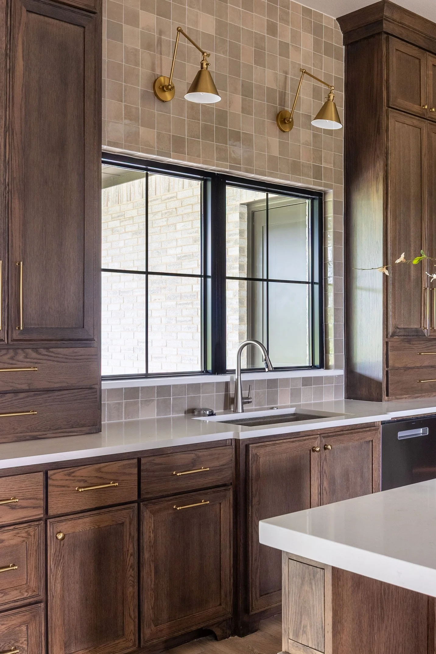 A kitchen featuring dark wood cabinetry, white quartz countertops, a window above the sink, and brass sconce lighting.