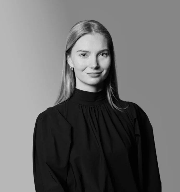Portret van een jonge vrouw met lang blond haar, zwarte jurk en oorbellen, grijs achtergrond, zwart-wit foto.