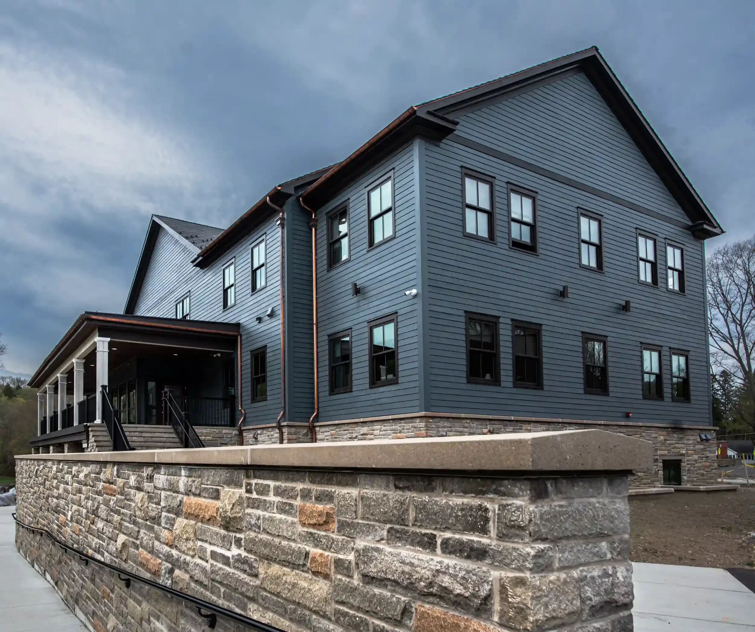 A multi-story house with grey siding, black-framed windows, and a stone foundation.