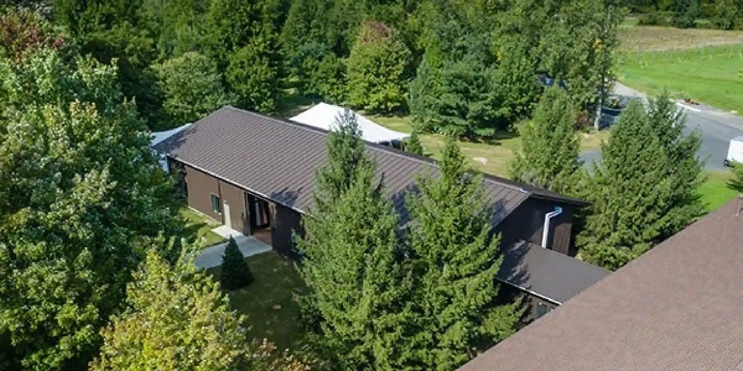 Aerial view of a house surrounded by dense trees with a sloped roof and a small lawn area.