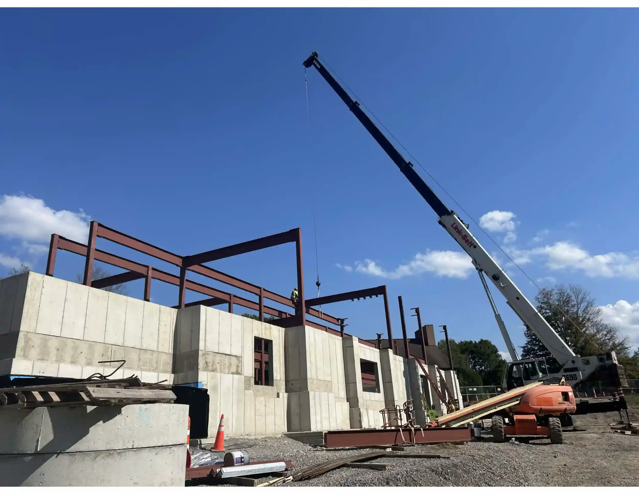Construction site with a crane lifting materials to a building under construction, with construction equipment visible.