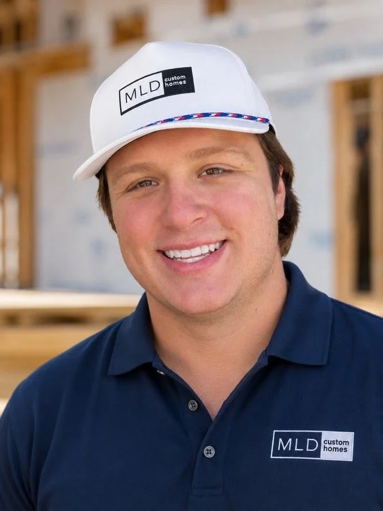 Jared Mcgee, Project Manager at MLD Custom Homes, smiles into the camera wearing a white hat and a navy blue shirt.