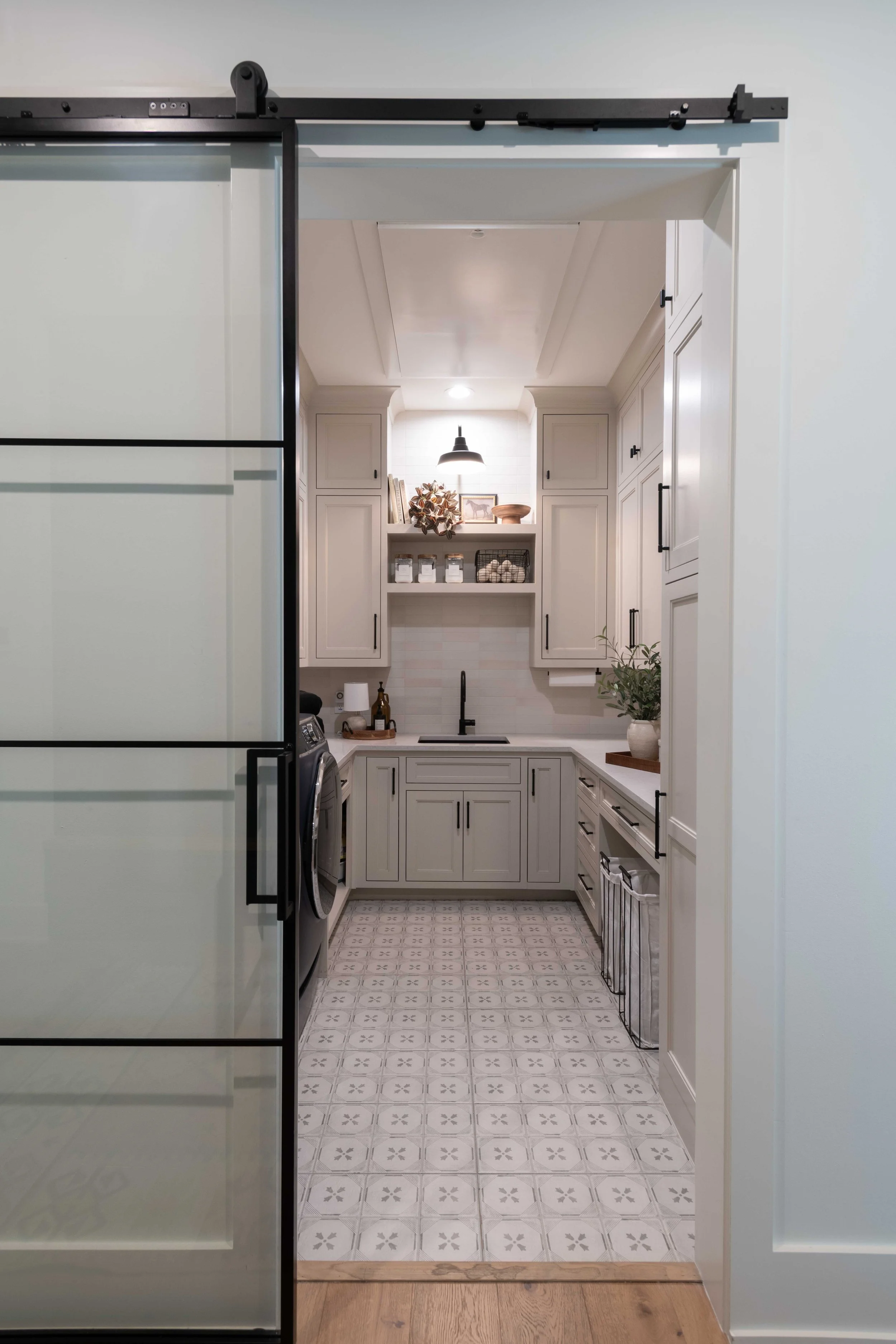 View of a cozy kitchen with white cabinetry, black hardware, patterned tile flooring, and decorative accents, visible through a frosted glass sliding door.