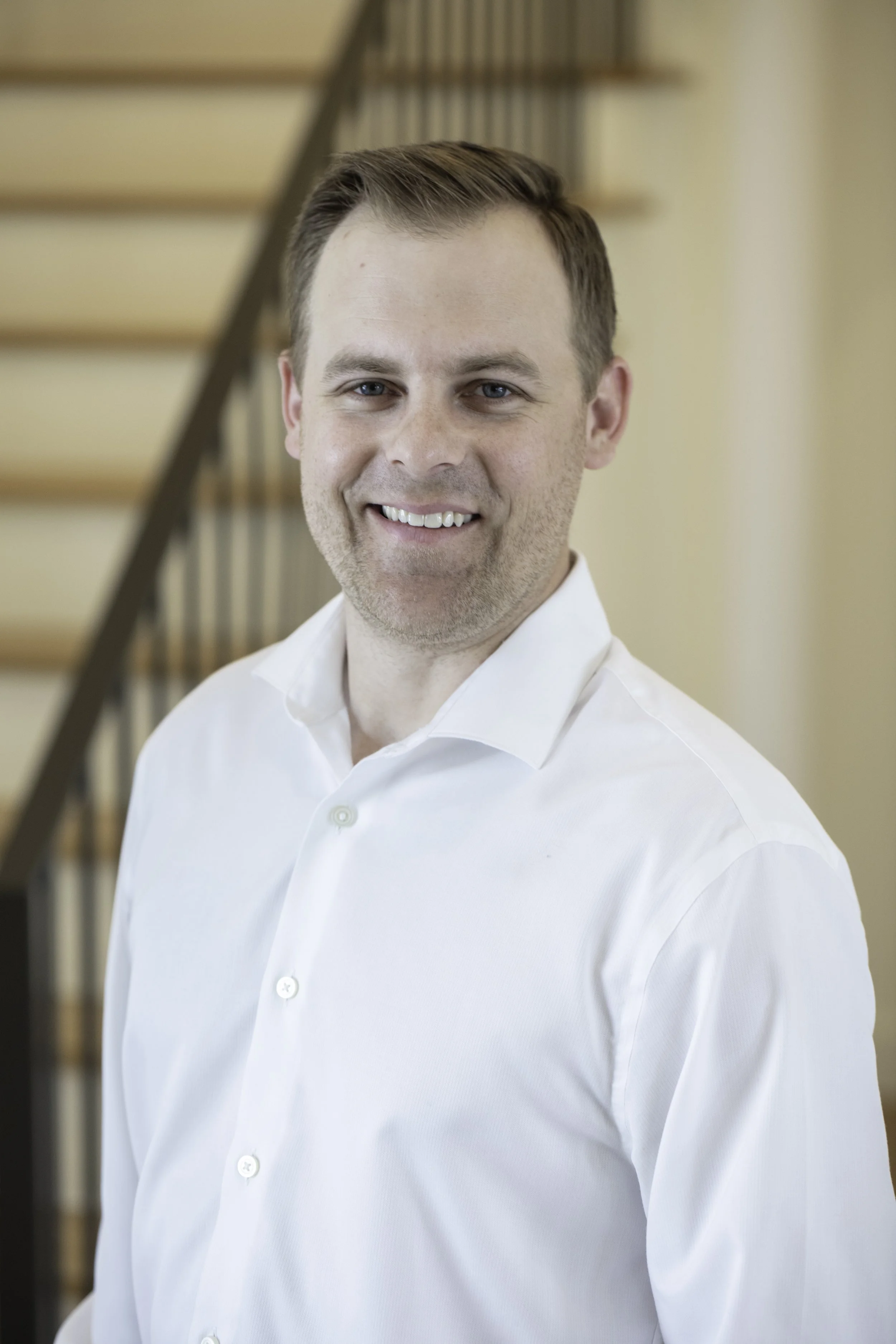 Landon Day, Founder of MLD Custom Homes, stands smiling in front of a staircase.