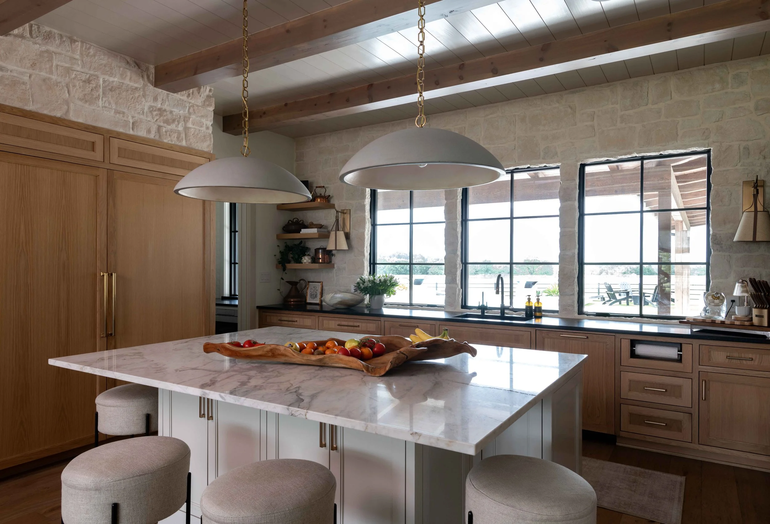 Modern kitchen with white marble island, wooden cabinets, large windows, and two dome pendant lights hanging from the ceiling.