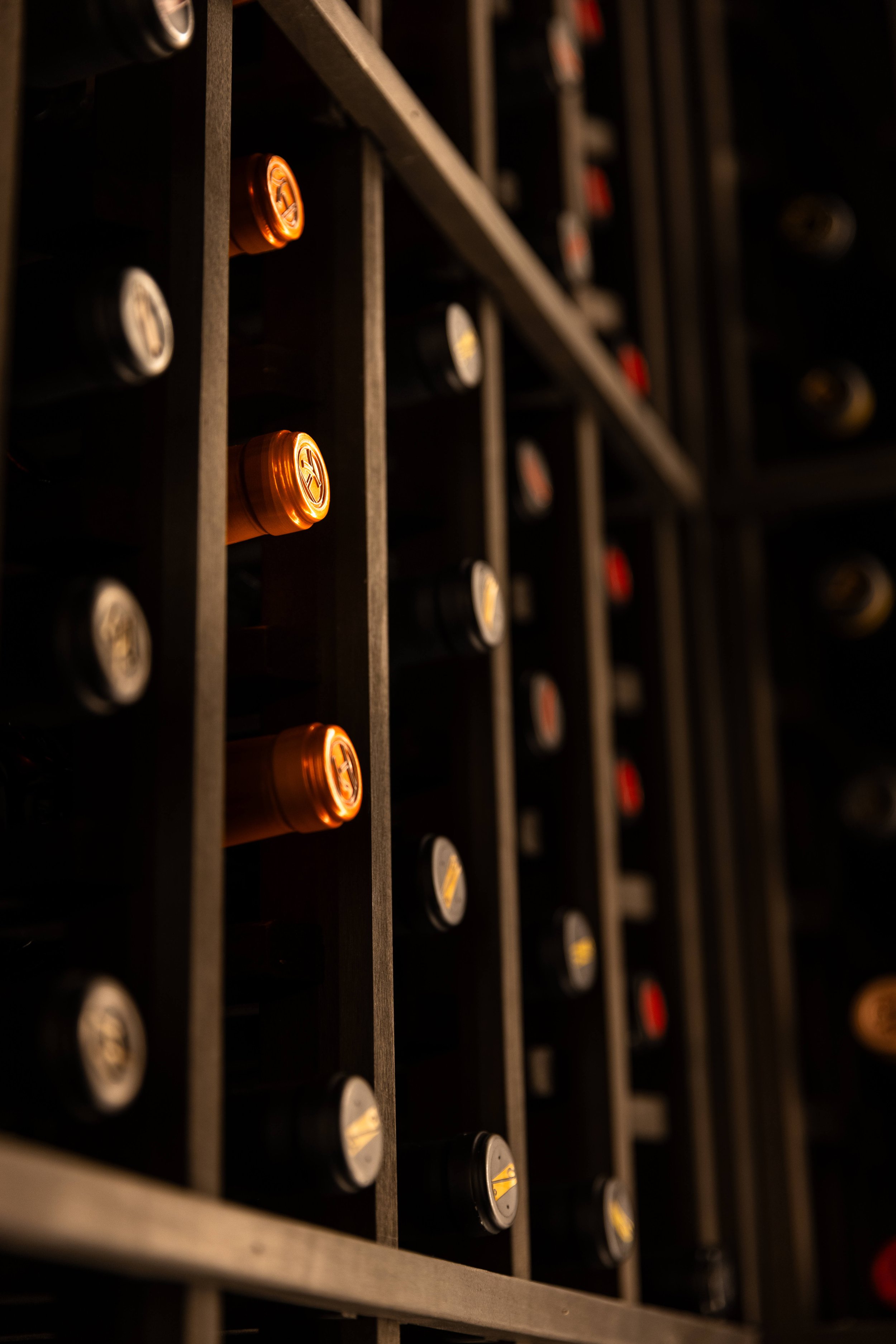 A close-up view of a wine rack with bottles stored horizontally. The focus is on the copper-colored bottle caps, with other bottles and caps blurred in the background.