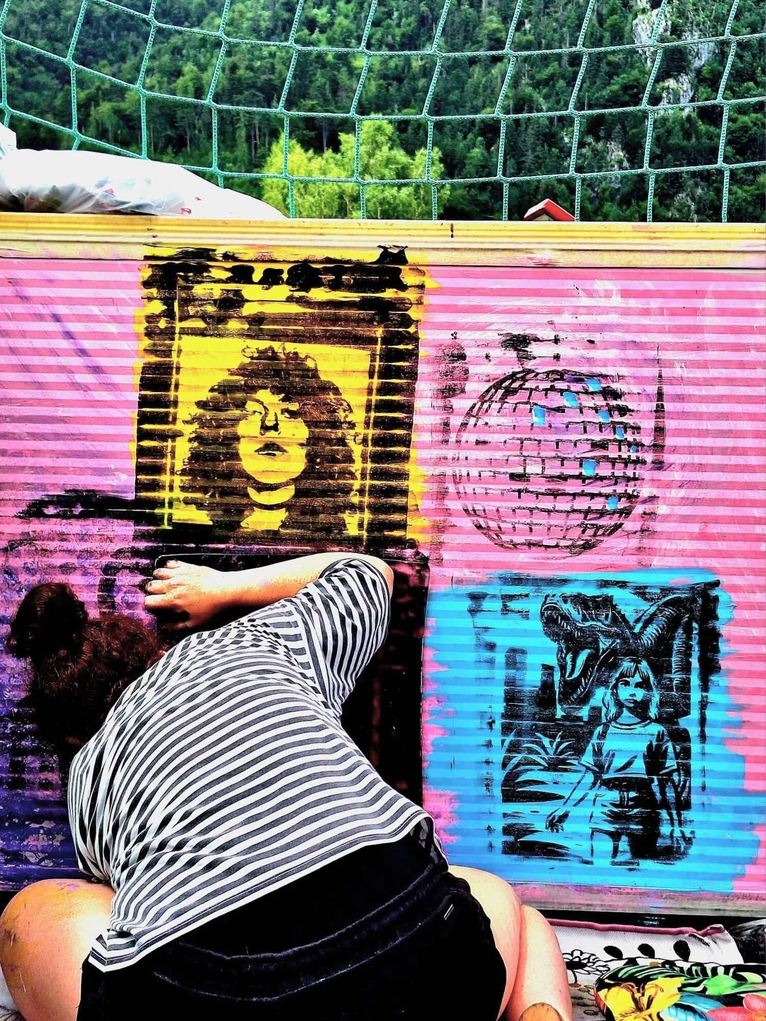 Straßenkunst mit mehreren Schichten von Street Art und Graffiti auf einer pinken Wand, mit einem Mensch in Shorts und gestreiftem Hemd, der auf dem Boden liegt.