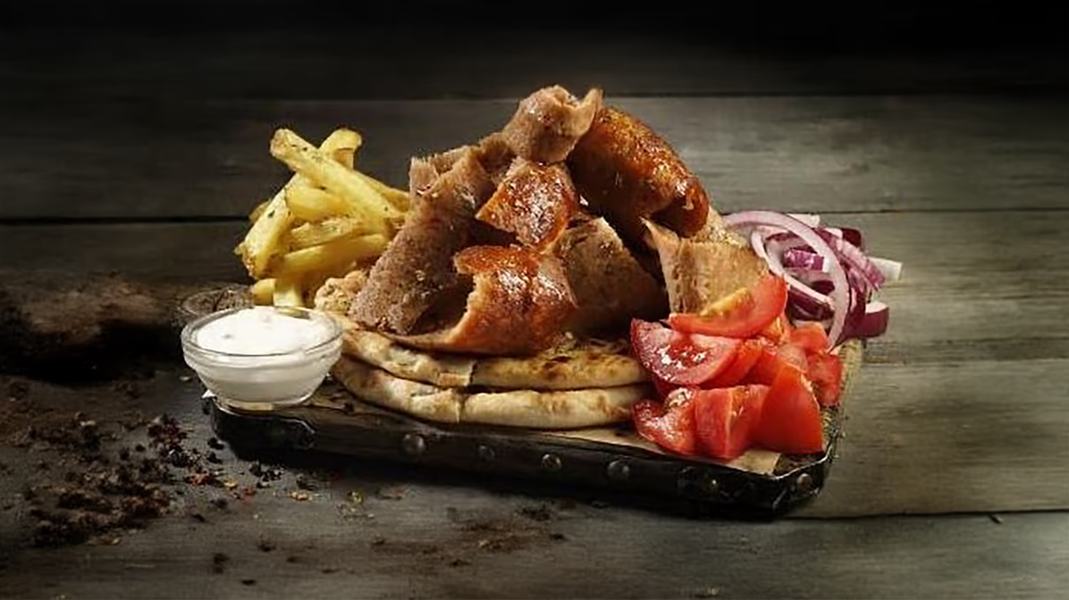 Fischfilets mit Pommes, Fladenbrot, Tomaten, Zwiebeln, und einer Sauce auf dunklem Holzuntergrund