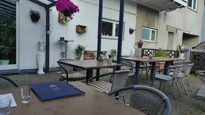 Ein Garten im Außenbereich mit mehreren Tischen und Stühlen, dabei sind Blumentöpfe und eine große weiße Skulptur sichtbar.