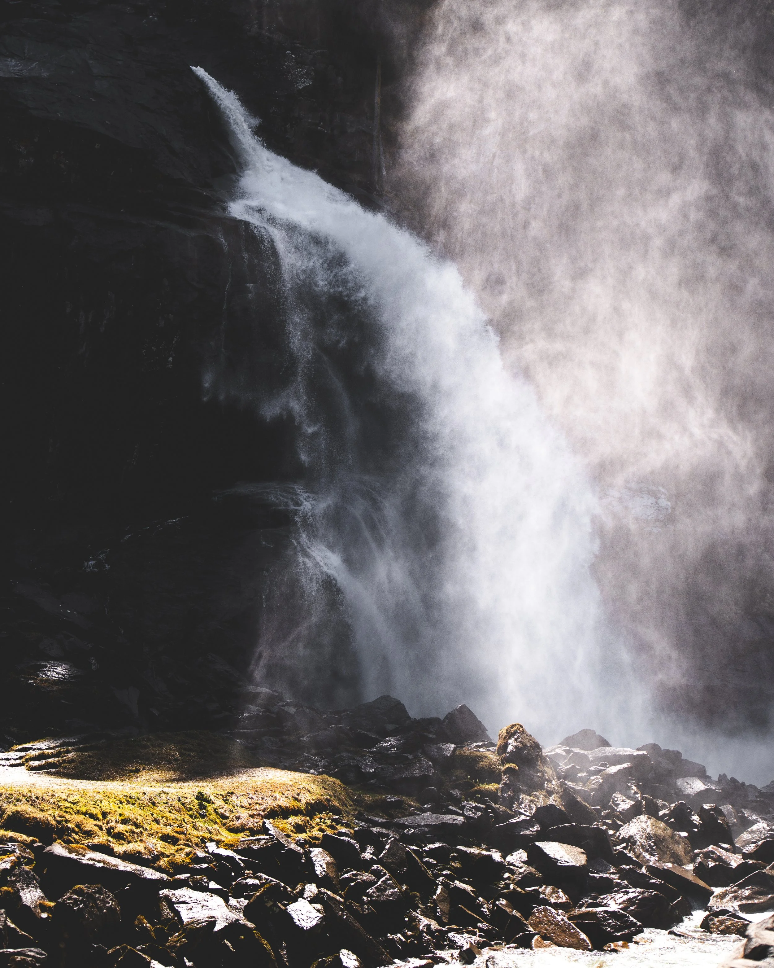 Ein Wasserfall stürzt von einer steilen Felswand in eine dunkle, felsige Umgebung, mit Wasser, das plätschert und auf den Boden prallt.