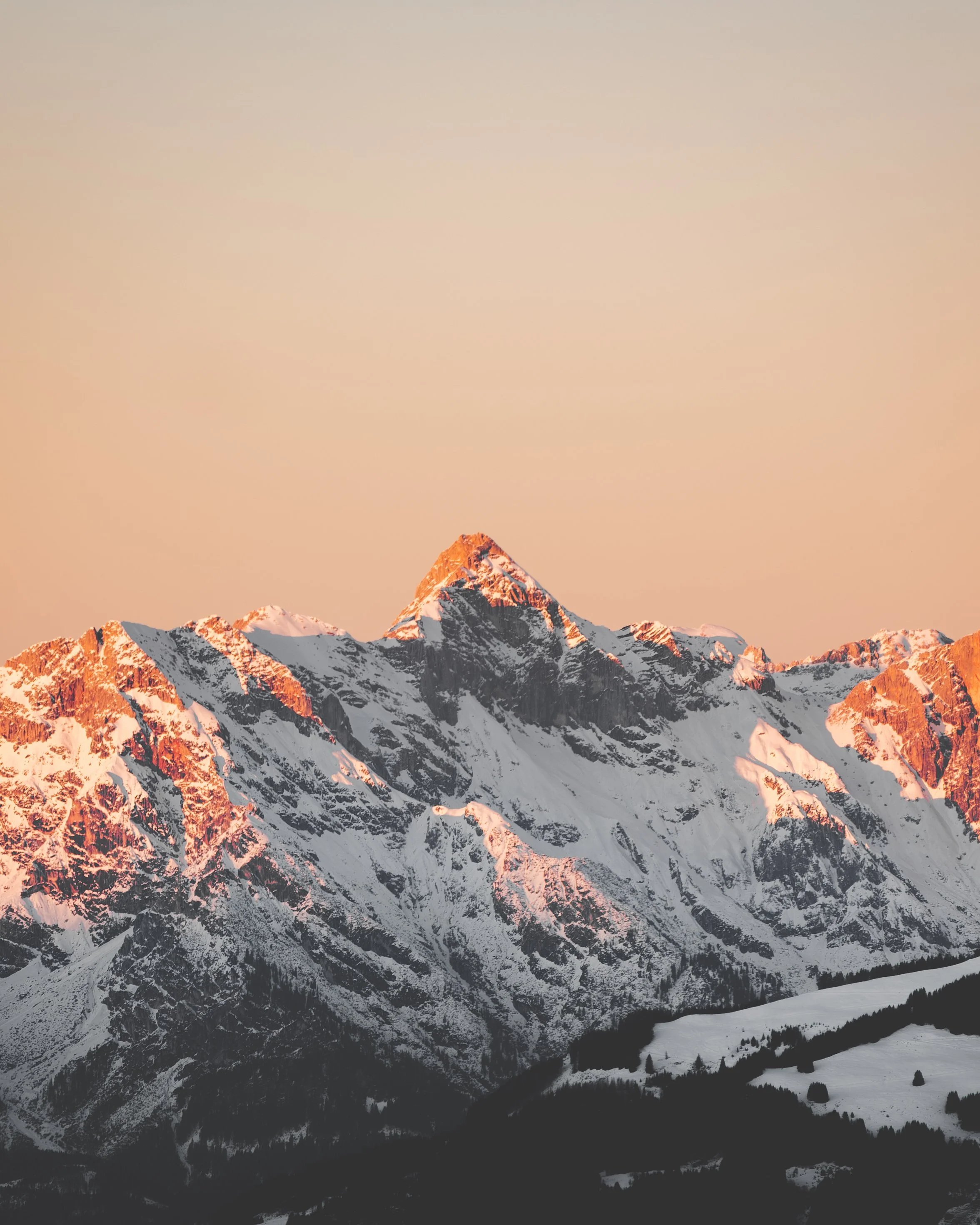 Berggipfel bei Sonnenuntergang mit Schneebedeckten Hängen und dunklen Foret in der Talsohle