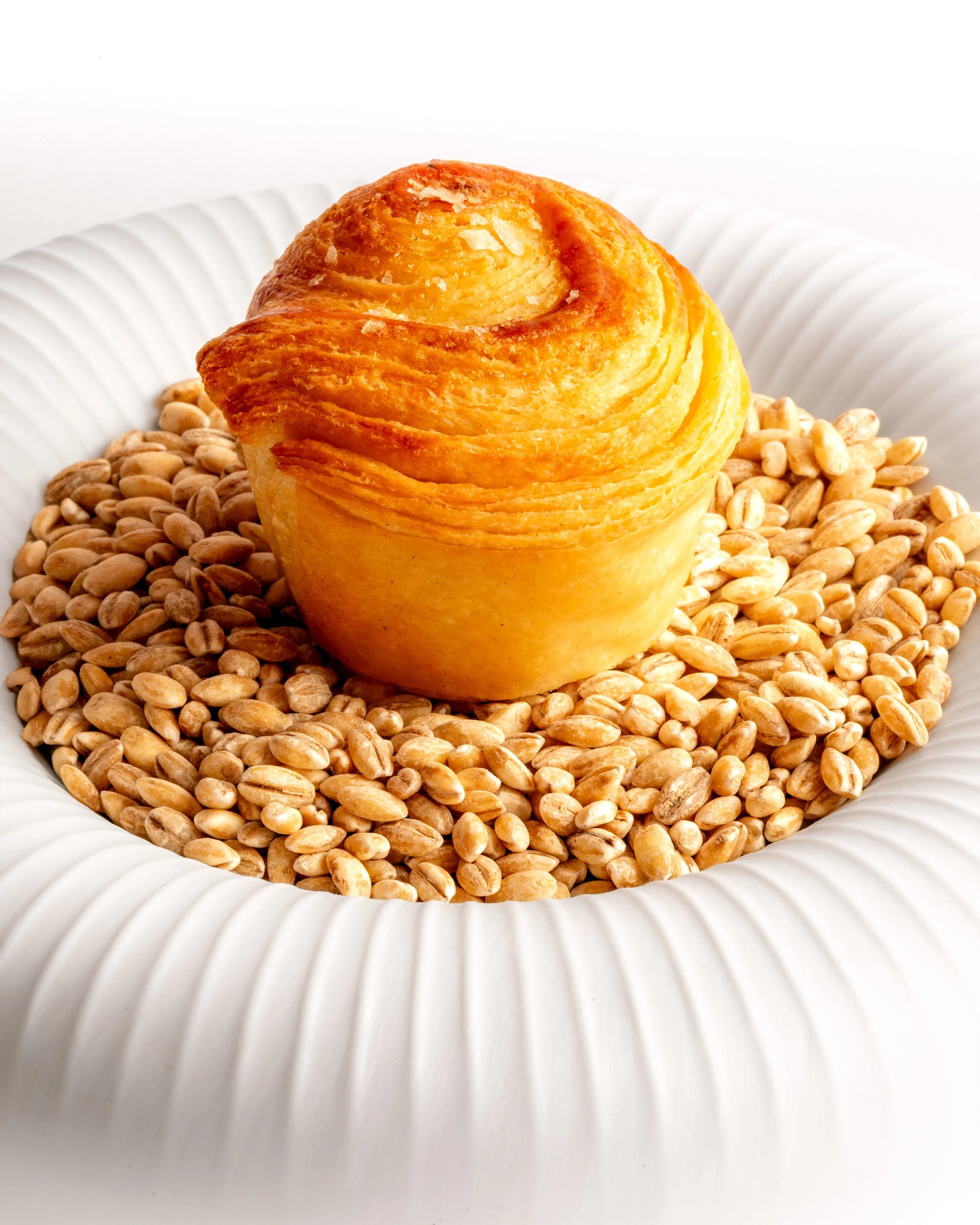 A pastry on a white, fluted plate, surrounded by sunflower seeds.