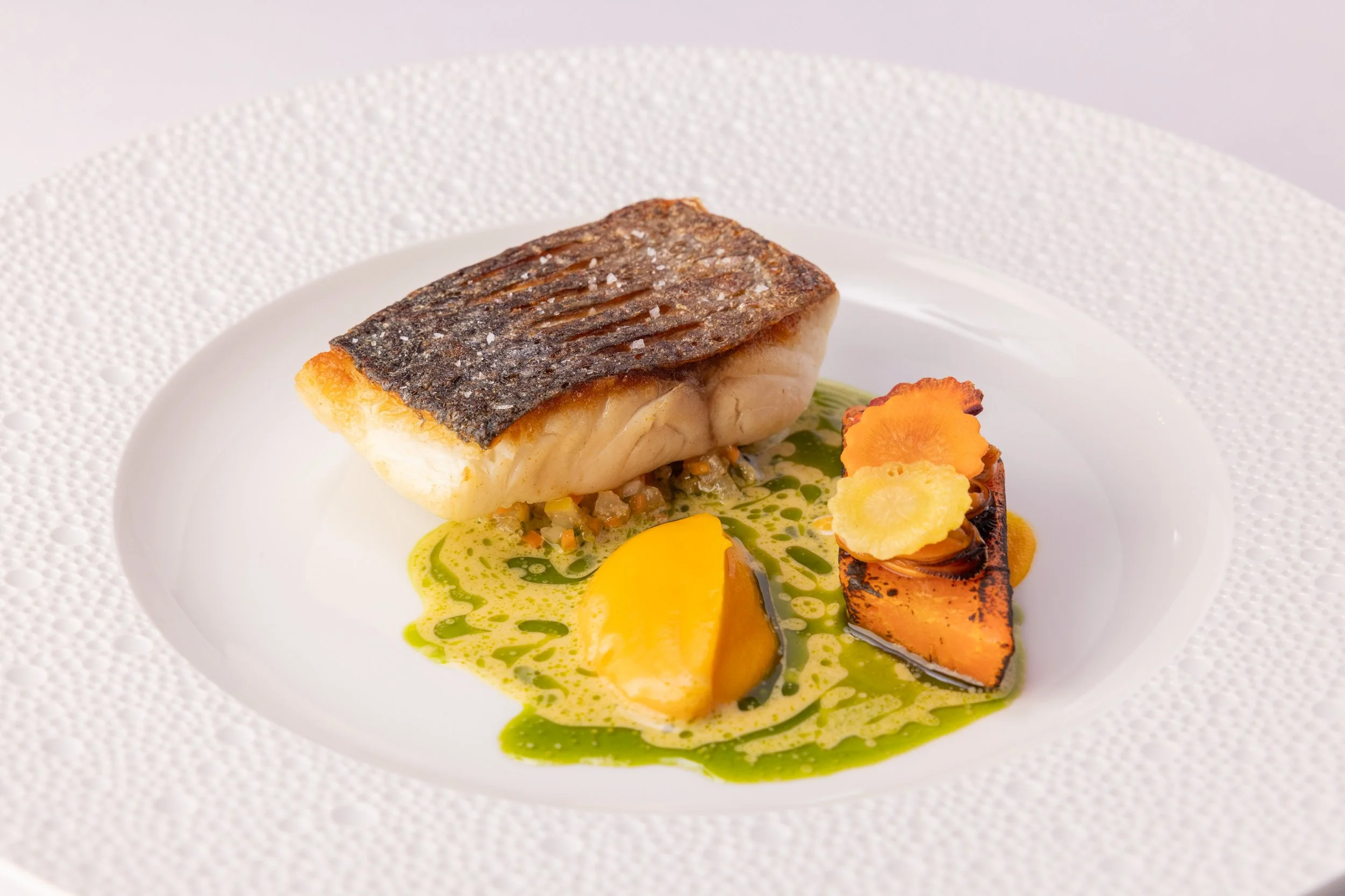 Plate with seared fish fillet, grilled vegetables, and green and yellow sauces