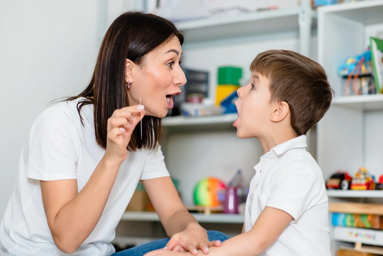 A speech therapist and a young boy are facing each other with their mouths open, working on learning correct tongue placement during myofunctional therapy for kids in Knoxville, TN.