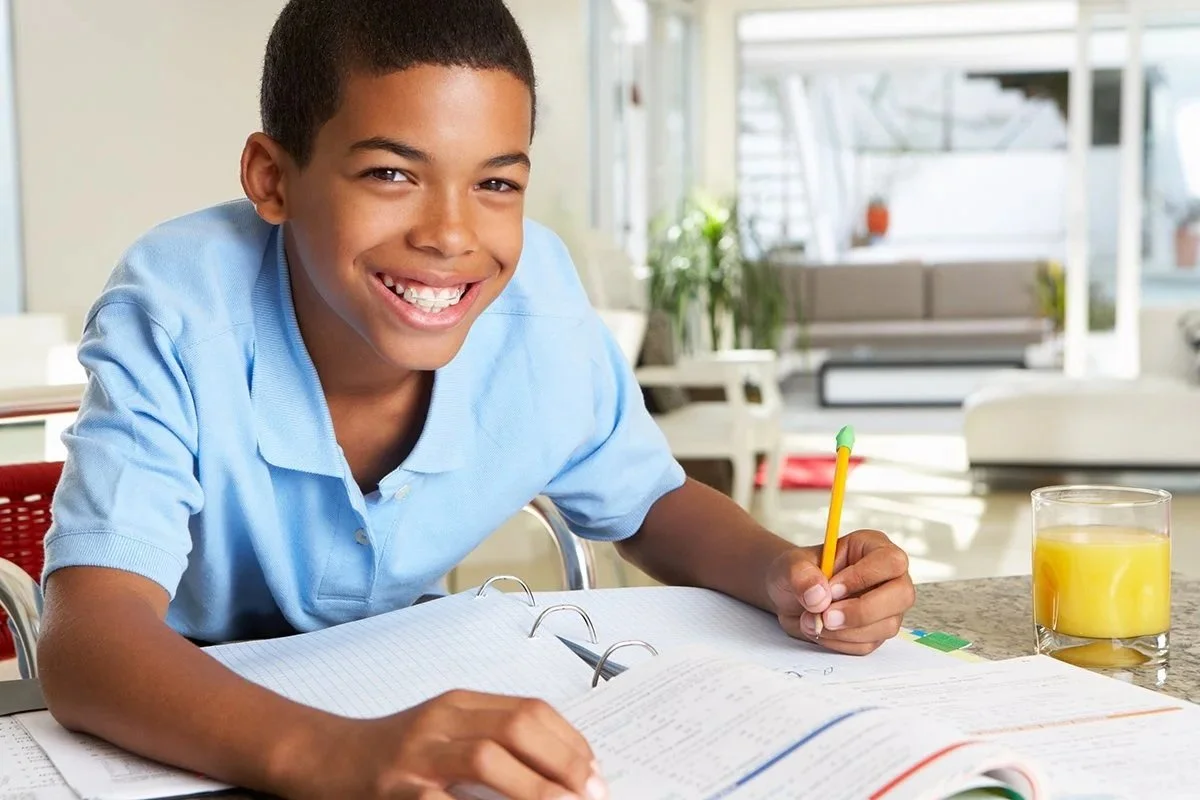 A young boy with dyslexia, smiling and sitting at a table with an open book, working on reading skills during literacy therapy for kids in Knoxville, TN.