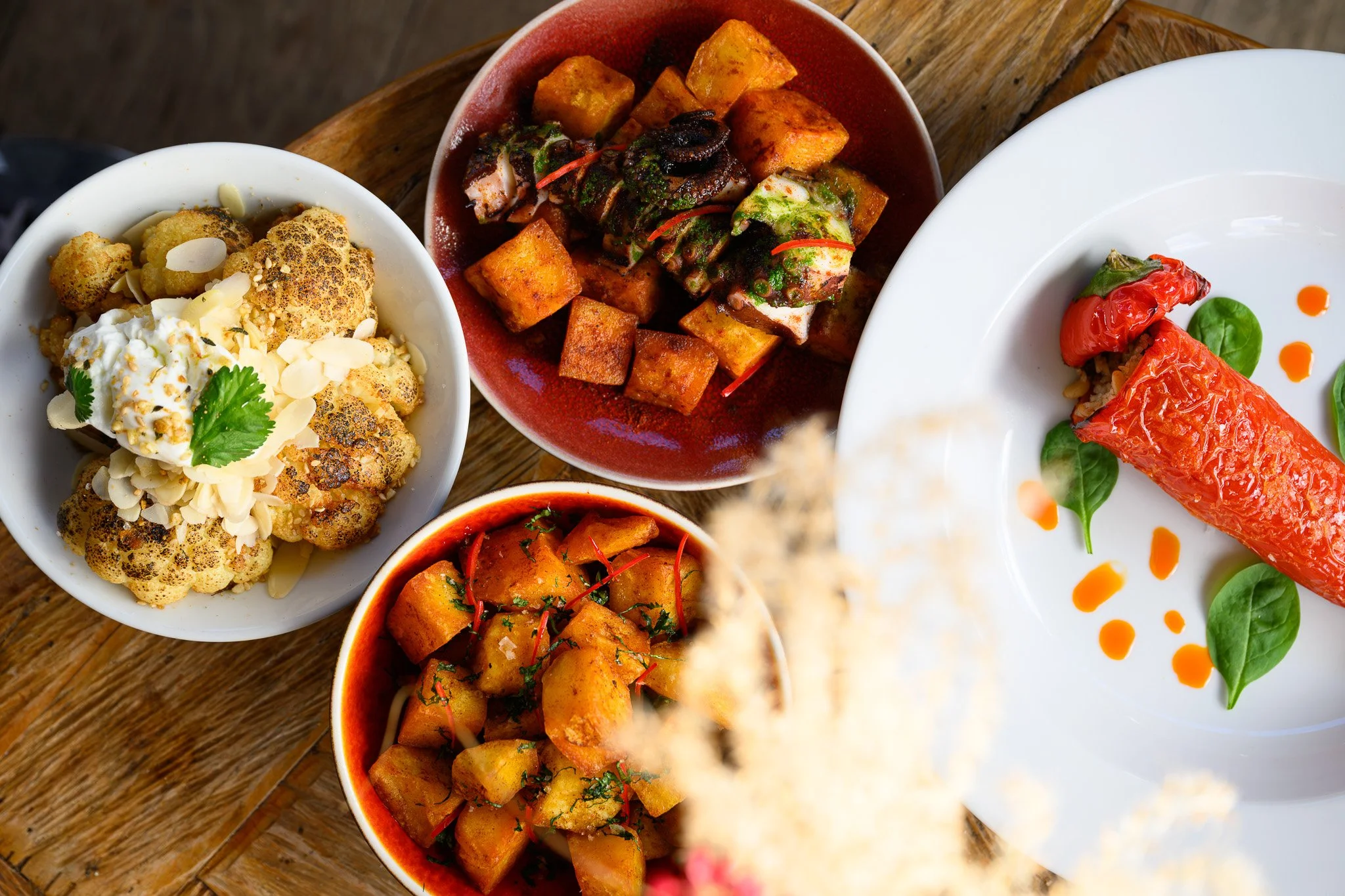 Assorted Indian dishes including cauliflower with almonds, spicy vegetable curry, and stuffed red peppers garnished with green leaves, served on a wooden table.