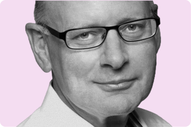 Close-up of a man with short hair, glasses, and a slight smile, wearing a collared shirt against a light lavender background.
