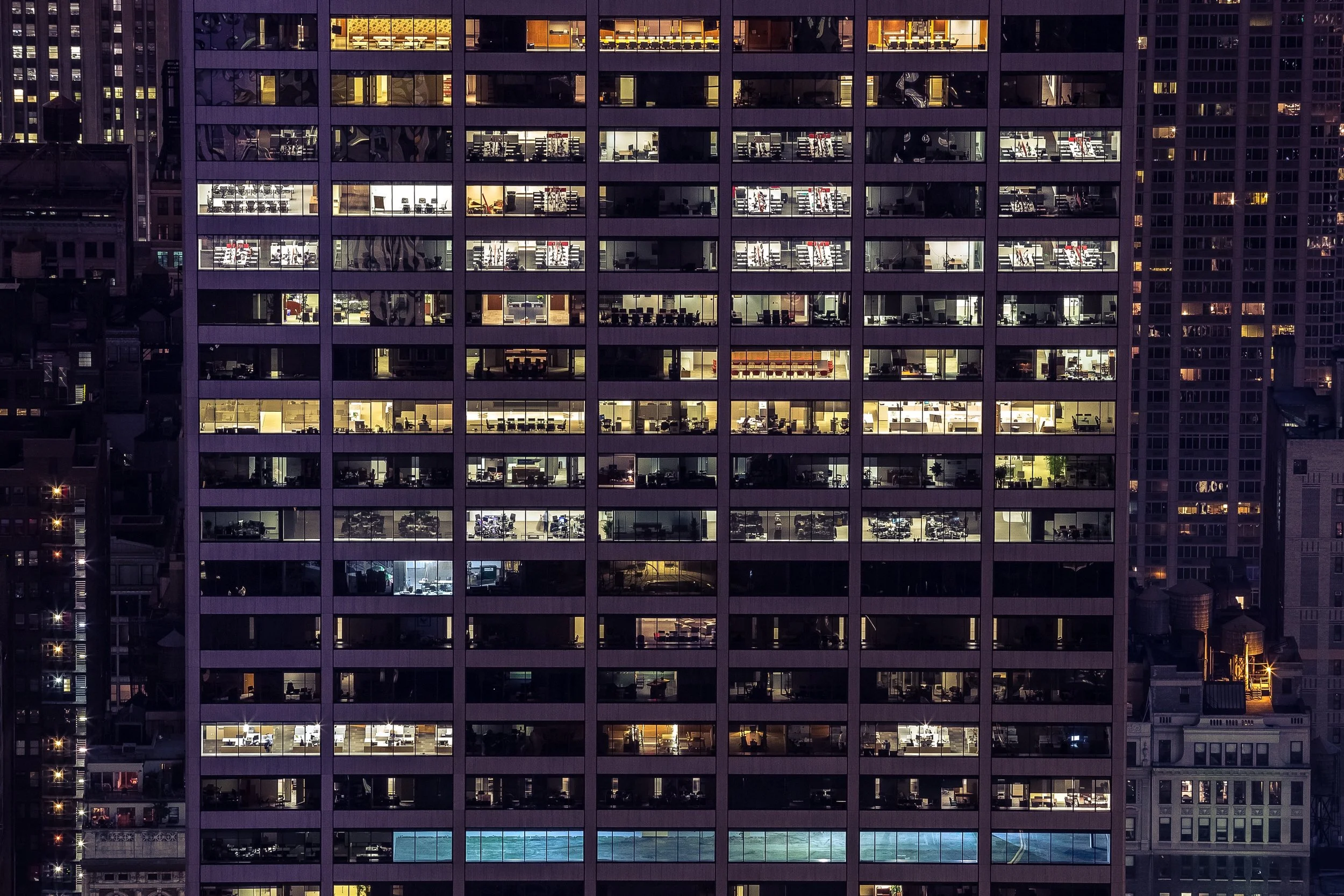 Nighttime view of a high-rise office building with illuminated office spaces visible through the windows.