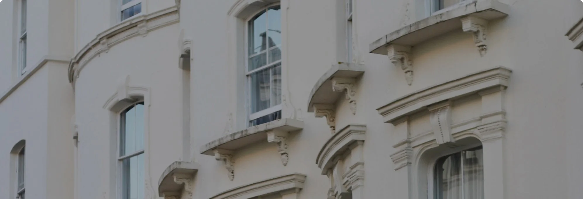 Close-up of the exterior of a beige or light-colored ornate apartment building with multiple windows and decorative architectural elements.