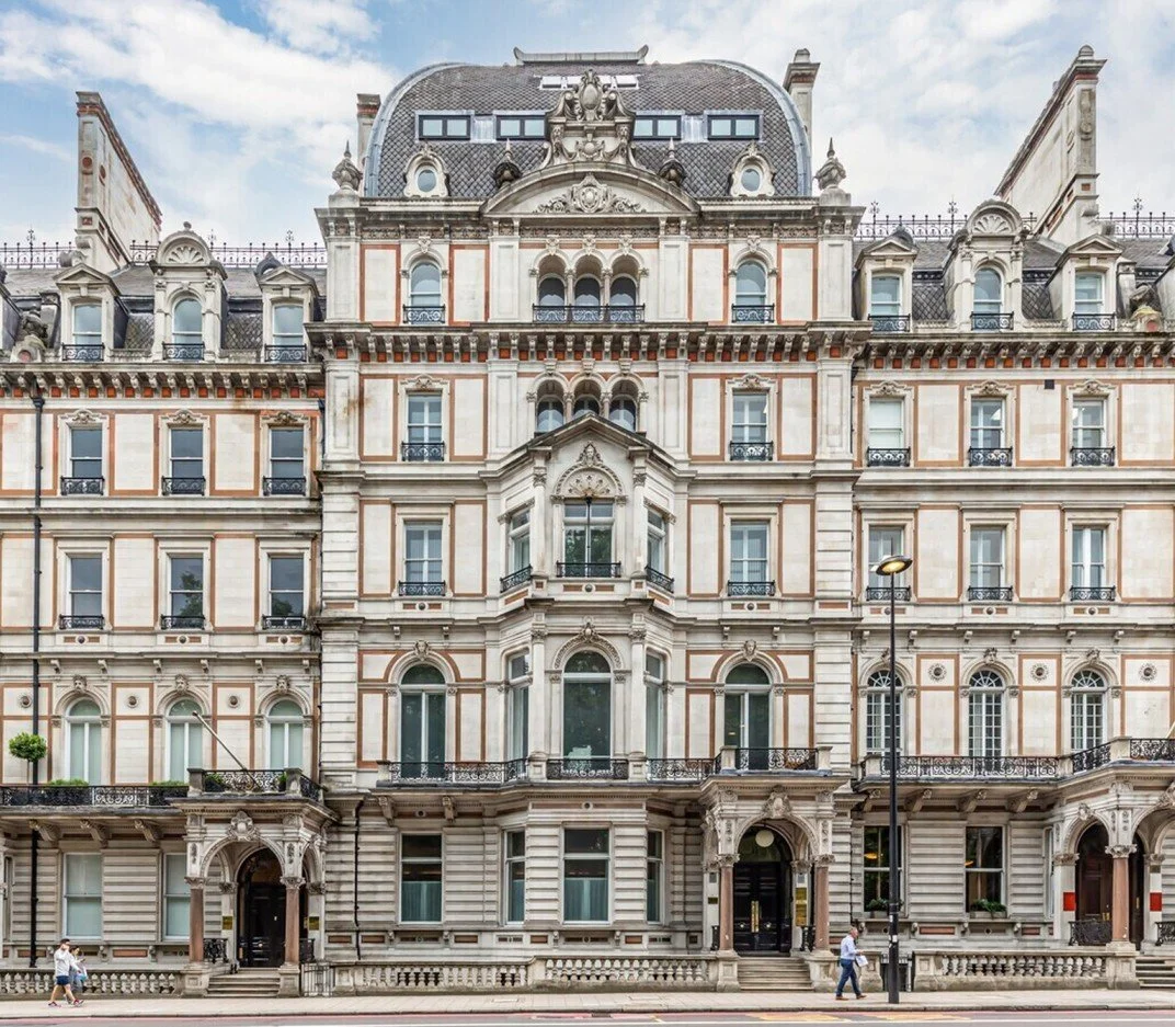 Historic multi-story building with ornate architectural details and mansard roof, situated on a city street with pedestrians and streetlights.