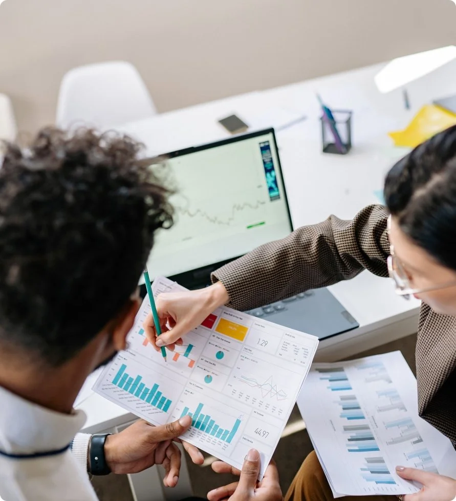 Two people working together reviewing financial reports with charts and graphs at a desk.
