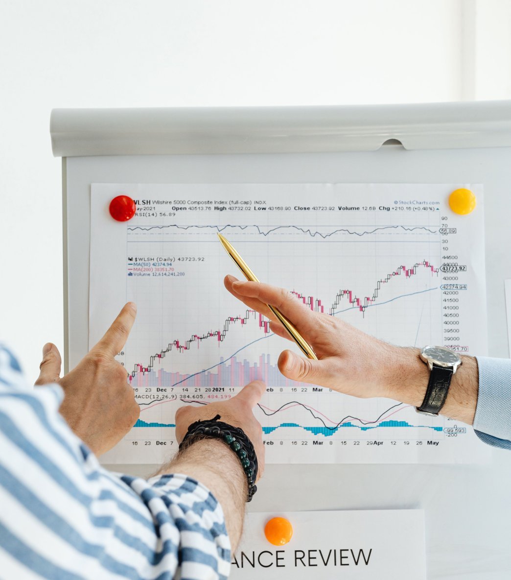 Two people analyzing a stock chart on a whiteboard, with one pointing and the other holding a gold pen, during a finance review.