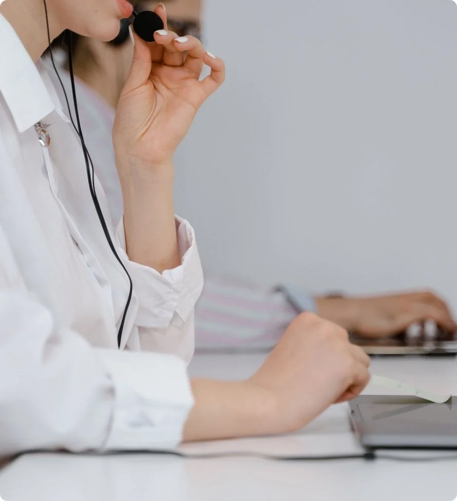 Close-up of a medical professional with a stethoscope holding a smartphone, sitting at a desk with a laptop and blurred background.