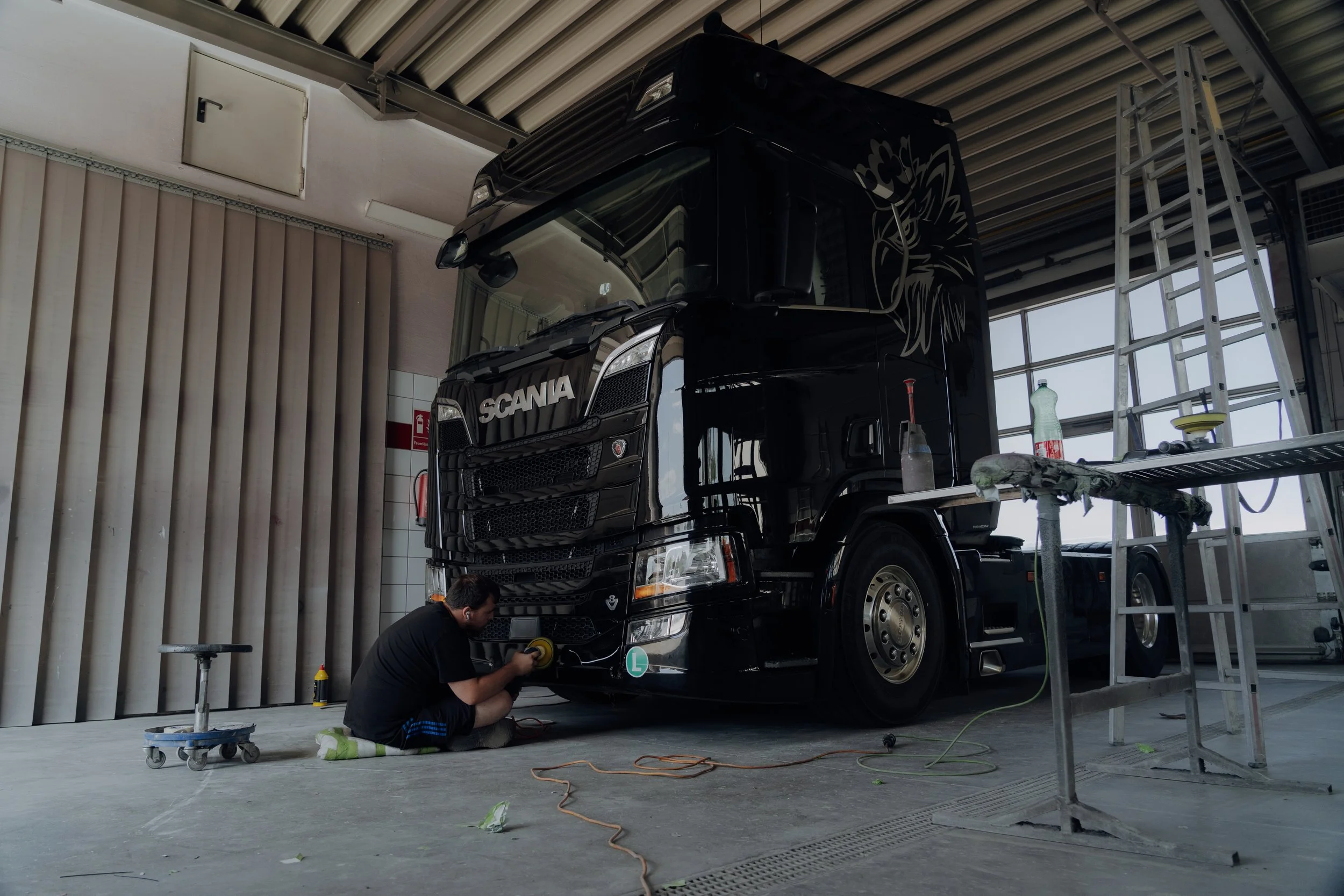 Ein Arbeiter poliert die Vorderseite eines schwarzen Trucks in einer Werkstatt.