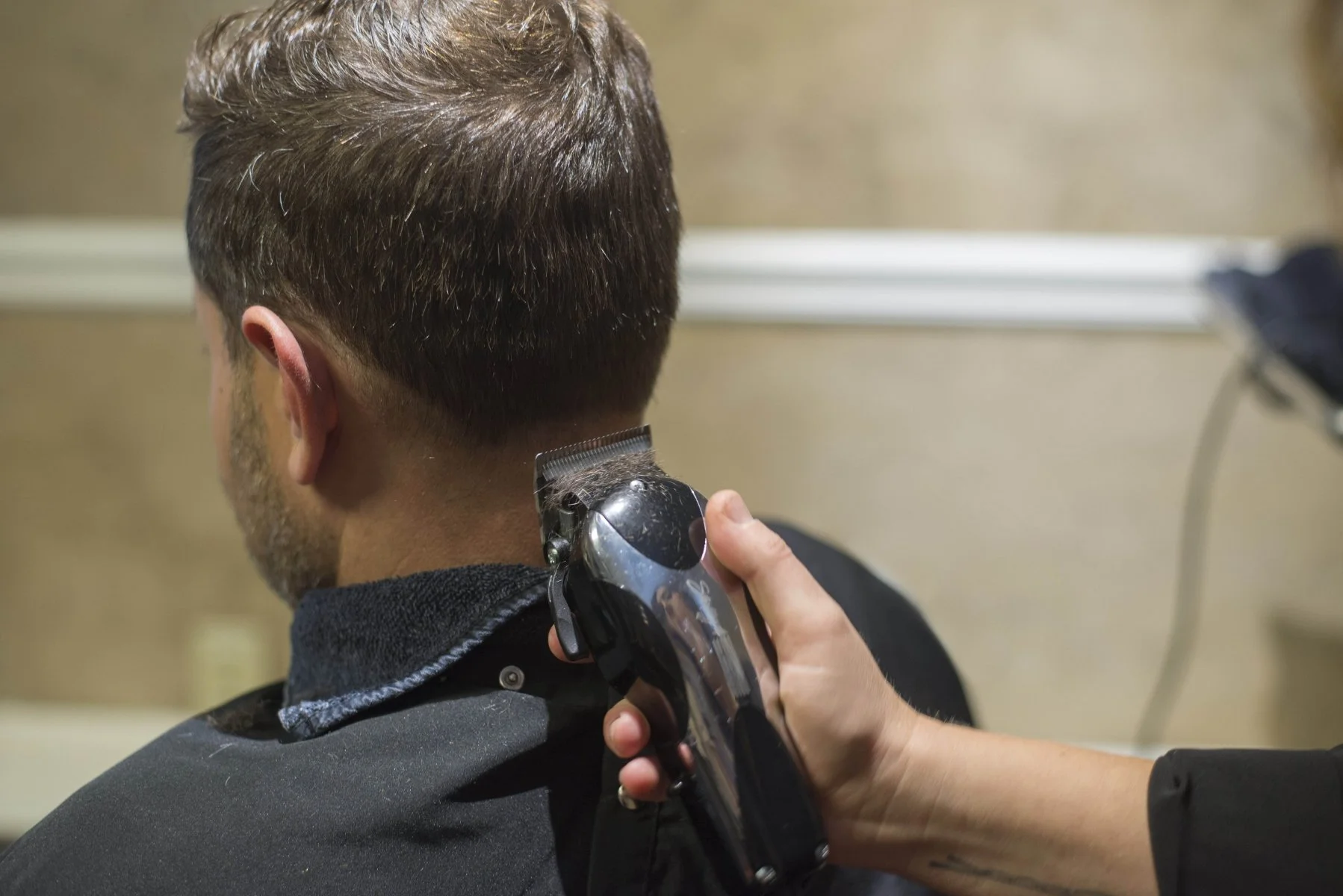A person gets a haircut with clippers at a barber's shop, with the barber using electric clippers on the back of the client's head.