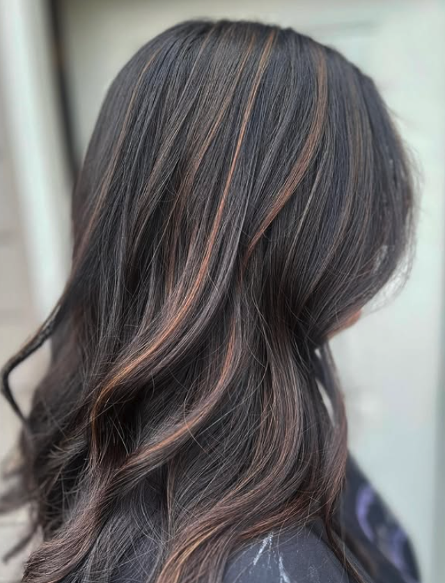 Close-up of wavy dark brown hair with caramel highlights.