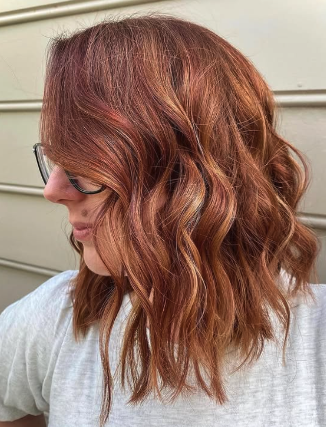Side view of a woman with shoulder-length wavy red hair wearing glasses and a white shirt.