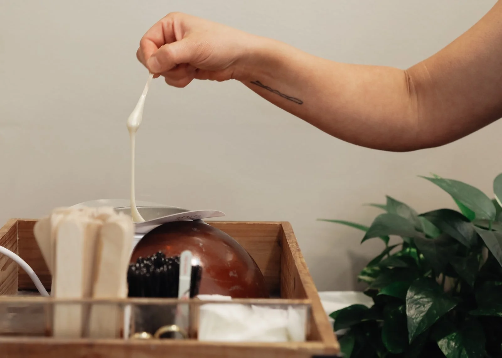 A person holding a cotton swab with what appears to be lotion or cream, with a small wooden organizer containing various items and a green leafy plant nearby.