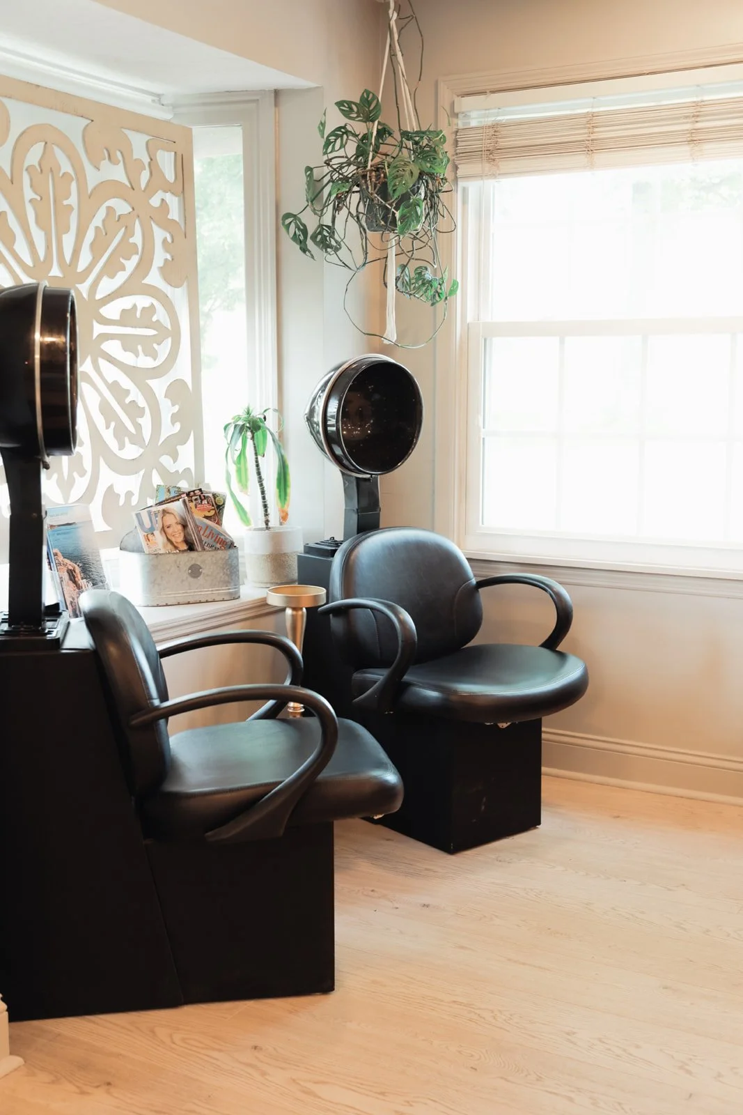 Salon with black chairs, hairdryer, magazines, indoor plants, large window, and decorative room divider.