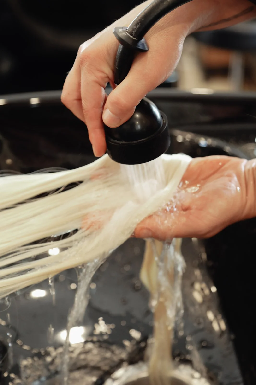 A person is rinsing a bundle of uncooked noodles under running water in a kitchen sink.