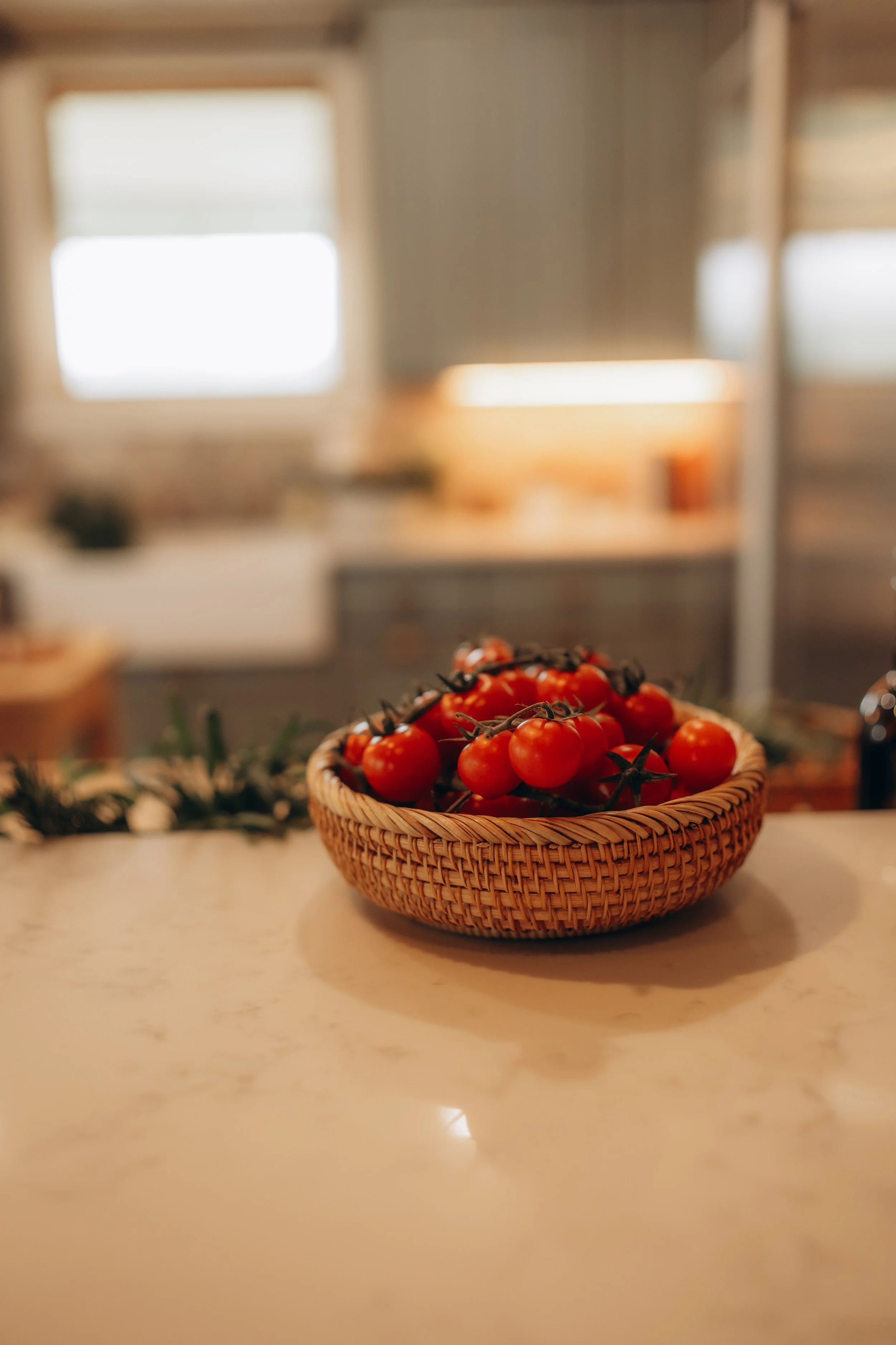 Basket of cherry tomatoes on a kitchen counter with a blurred background of windows and wooden house interior.