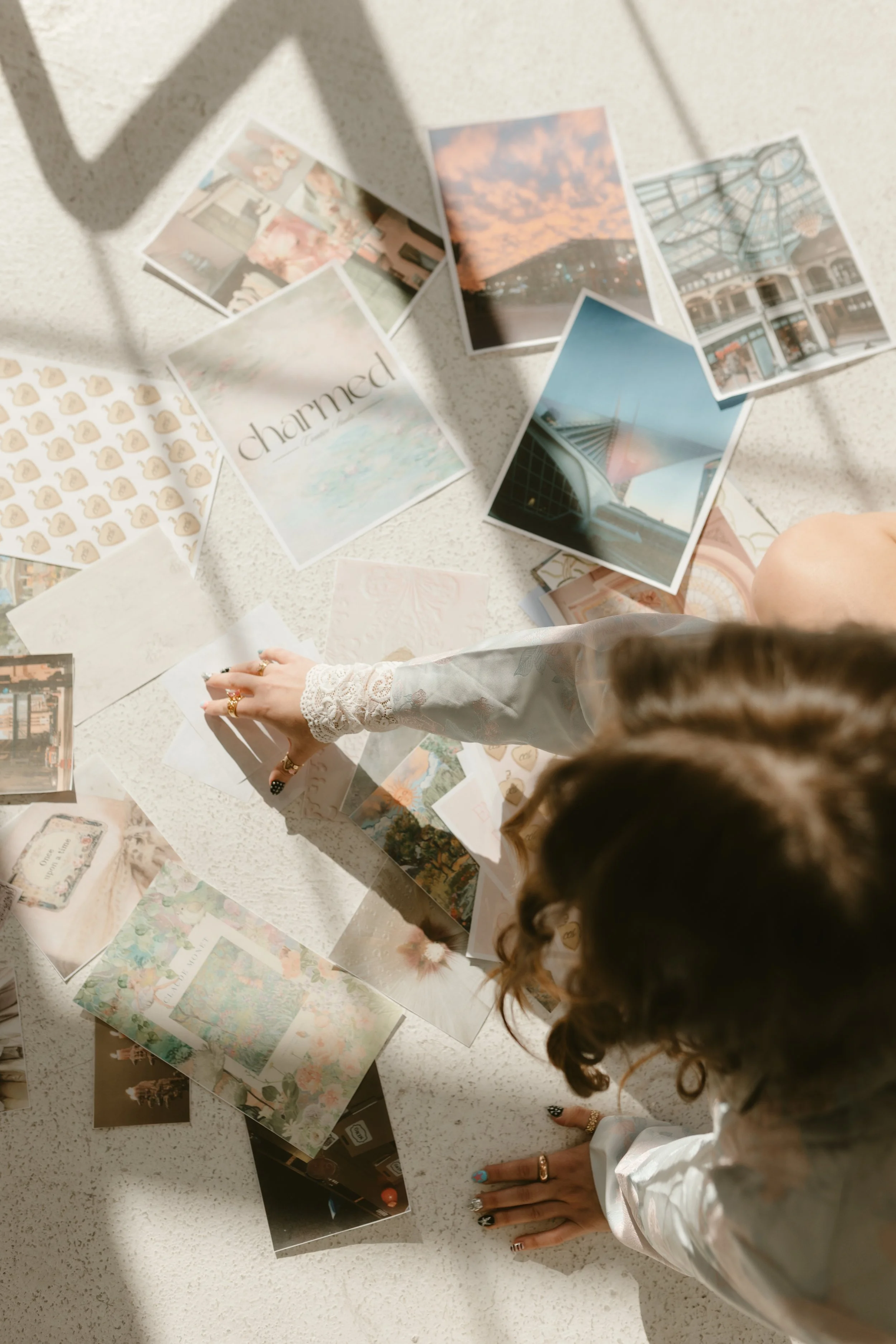 Person with wavy hair and decorated nails arranging postcards and photographs on a table.