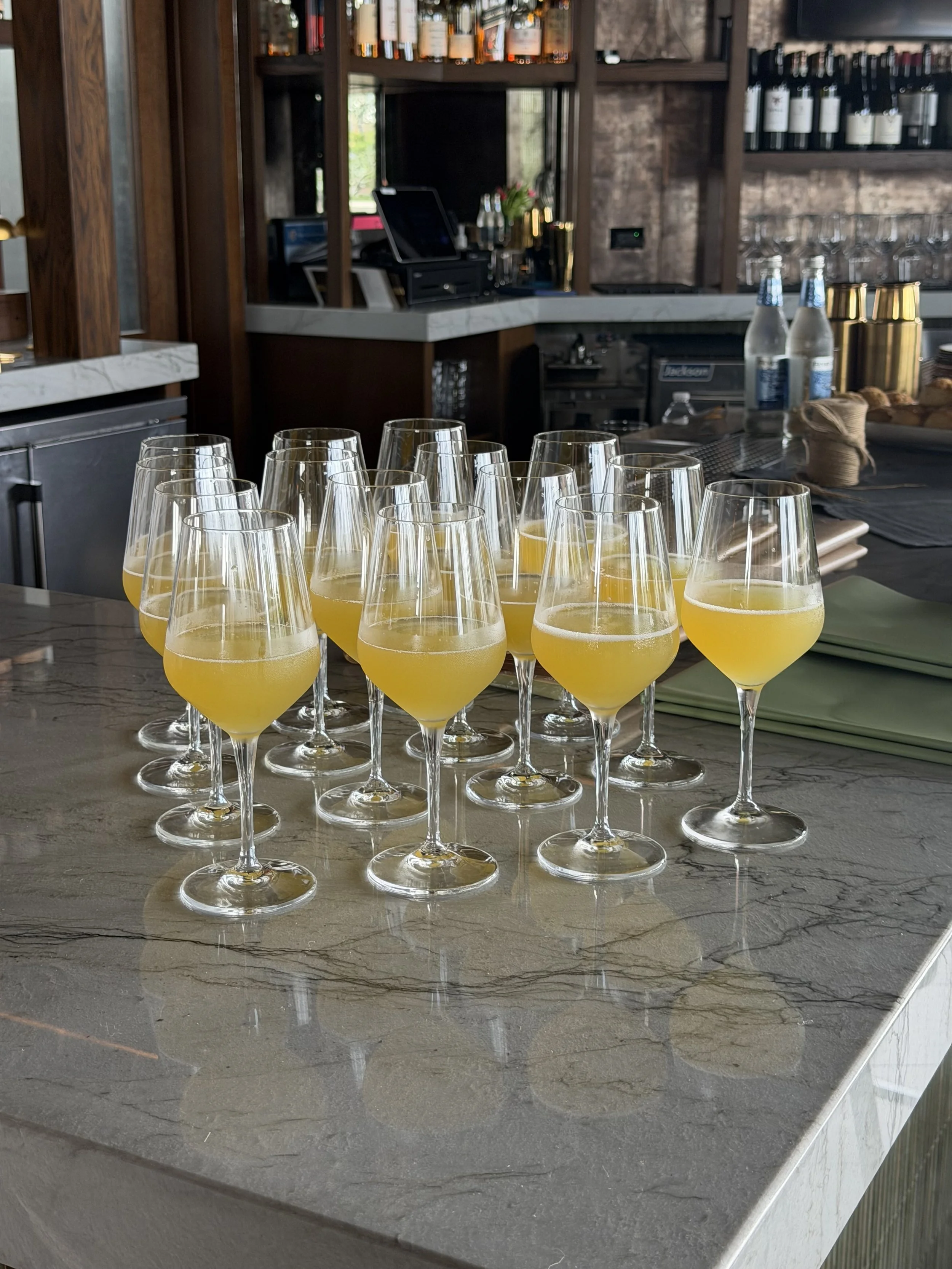 Multiple glasses of mimosa with orange juice on a marble countertop in a bar or restaurant setting.