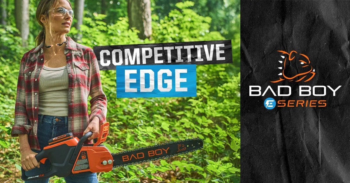 A woman outdoors in a wooded area holding an orange and black chainsaw labeled "Bad Boy". The scene features text "Competitive Edge" and a logo for "Bad Boy" Series.