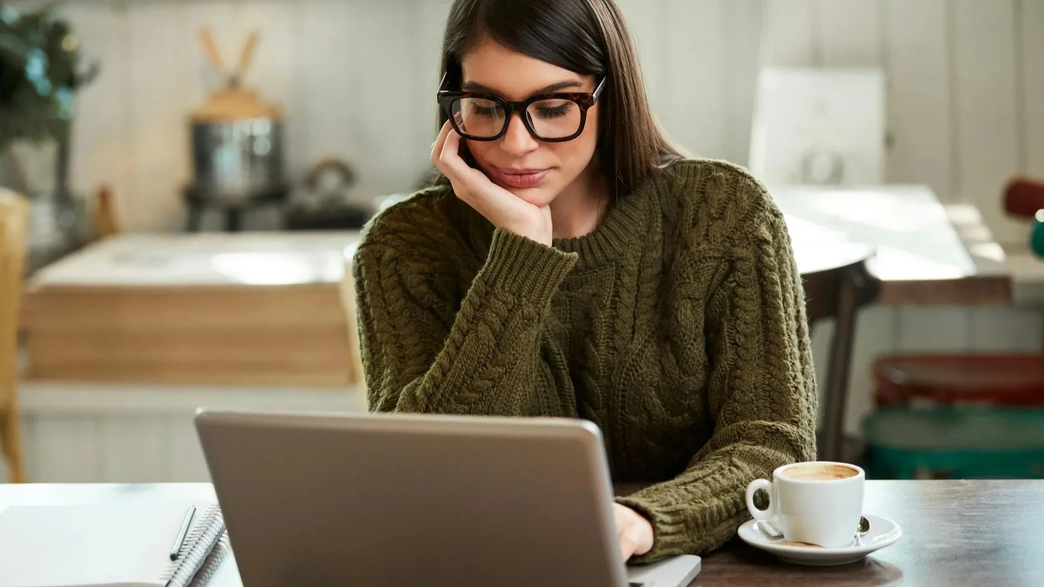 Woman sitting with a coffee doing work on a laptop.