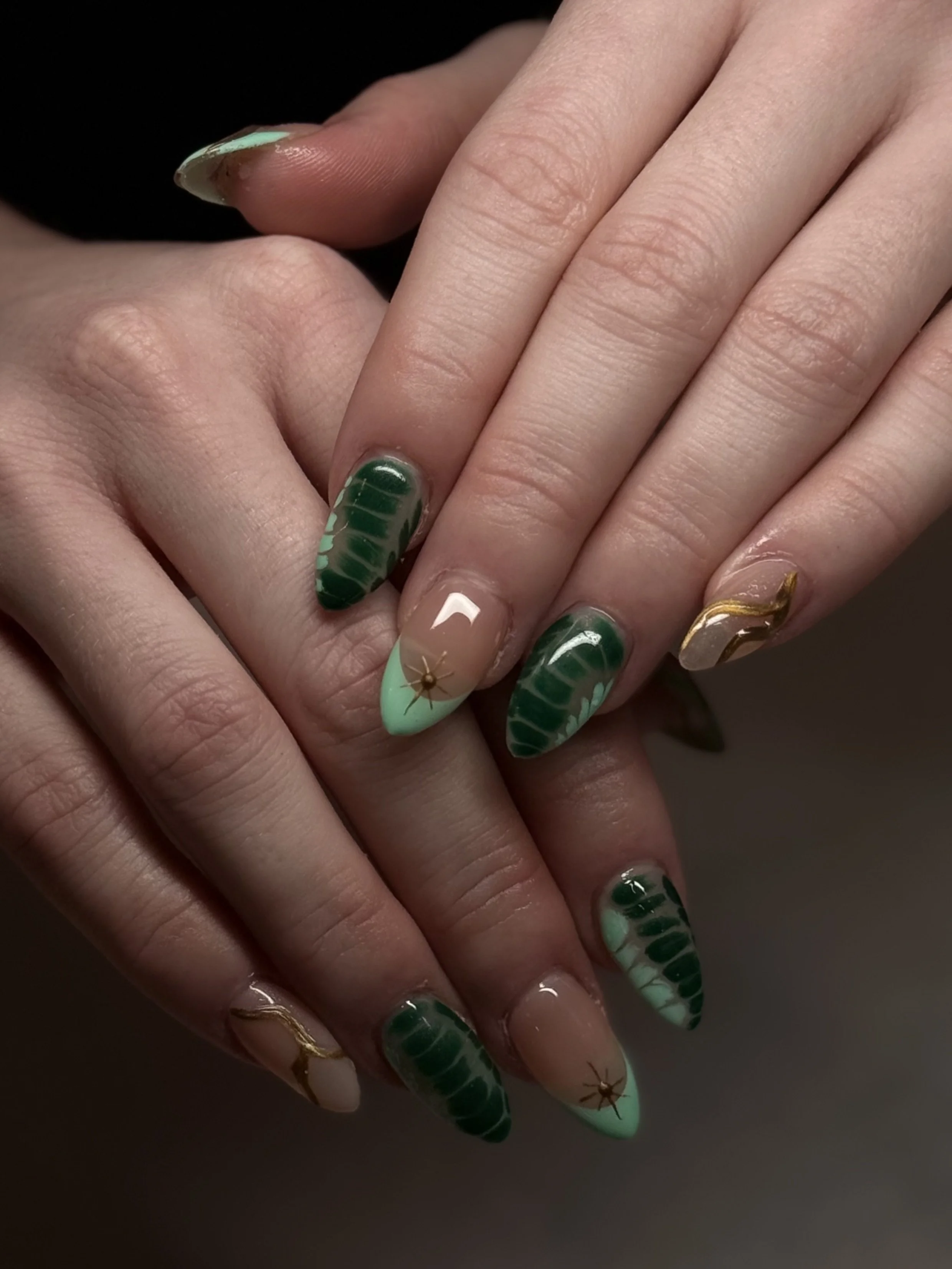 Close-up of a hand with manicured nails featuring green, white, and clear polish with gold accents and star designs.