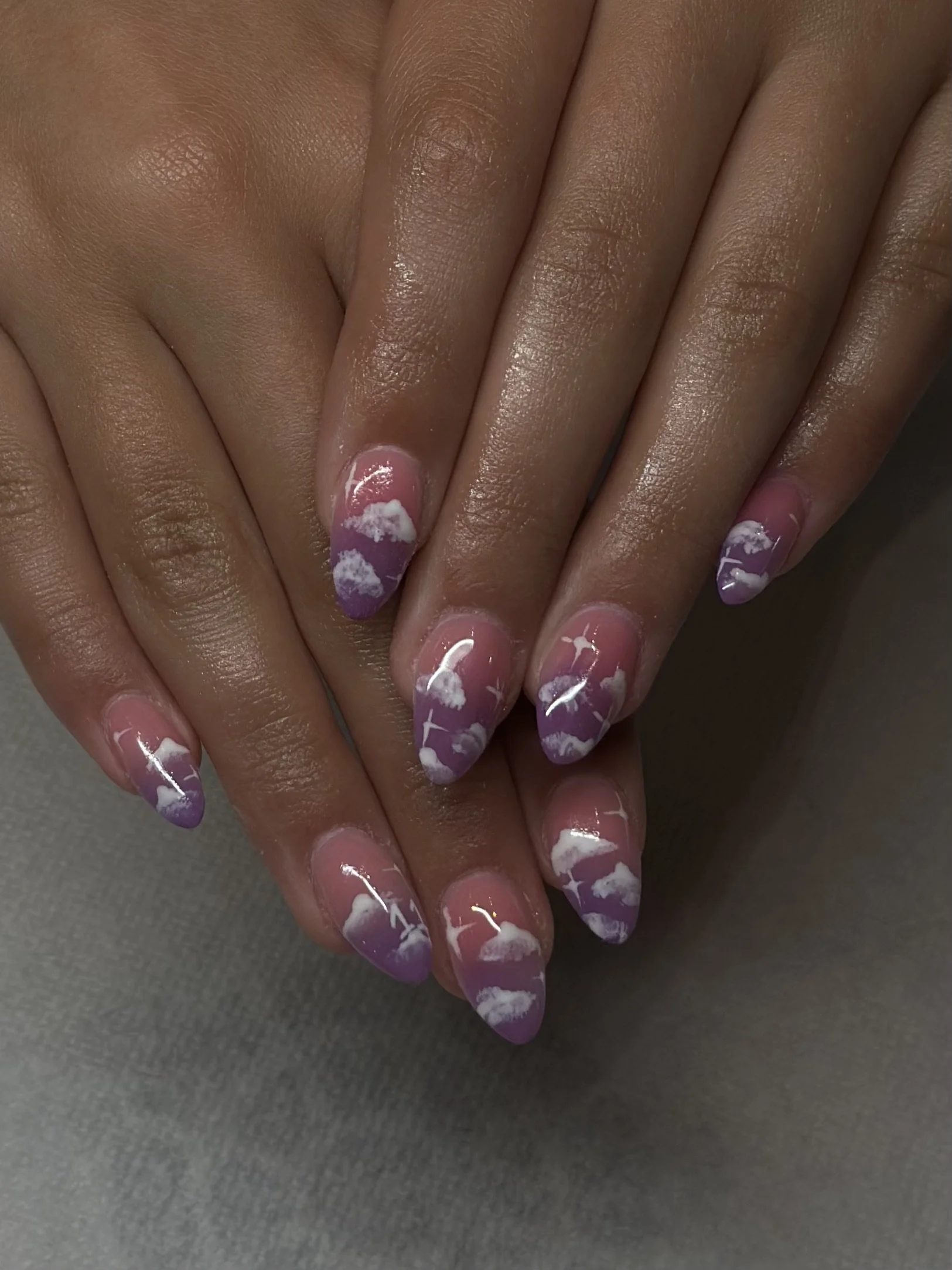Close-up of hands with manicured nails painted in a purple and white cloud design.