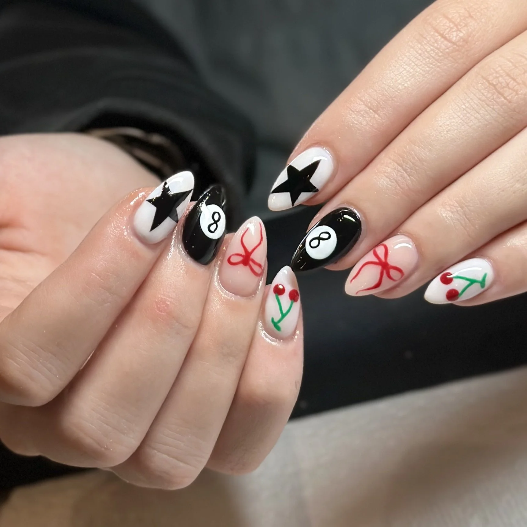 Close-up of a person's hand with Christmas-themed nail art, including black stars, red bows, cherries, and the numbers 8 and 1 on their nails.