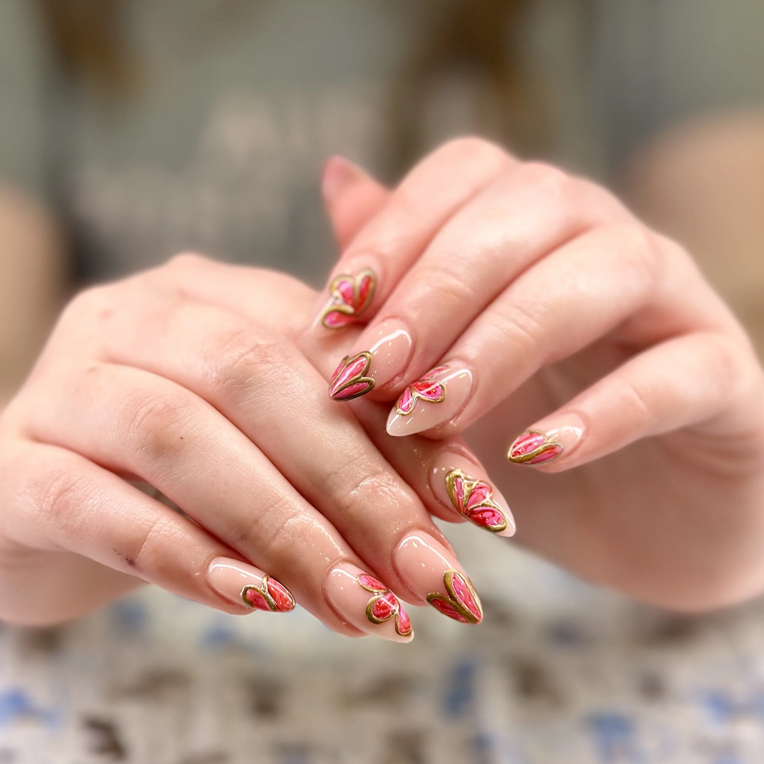 Close-up of a person's hand with decorated fingernails featuring pink and gold designs.