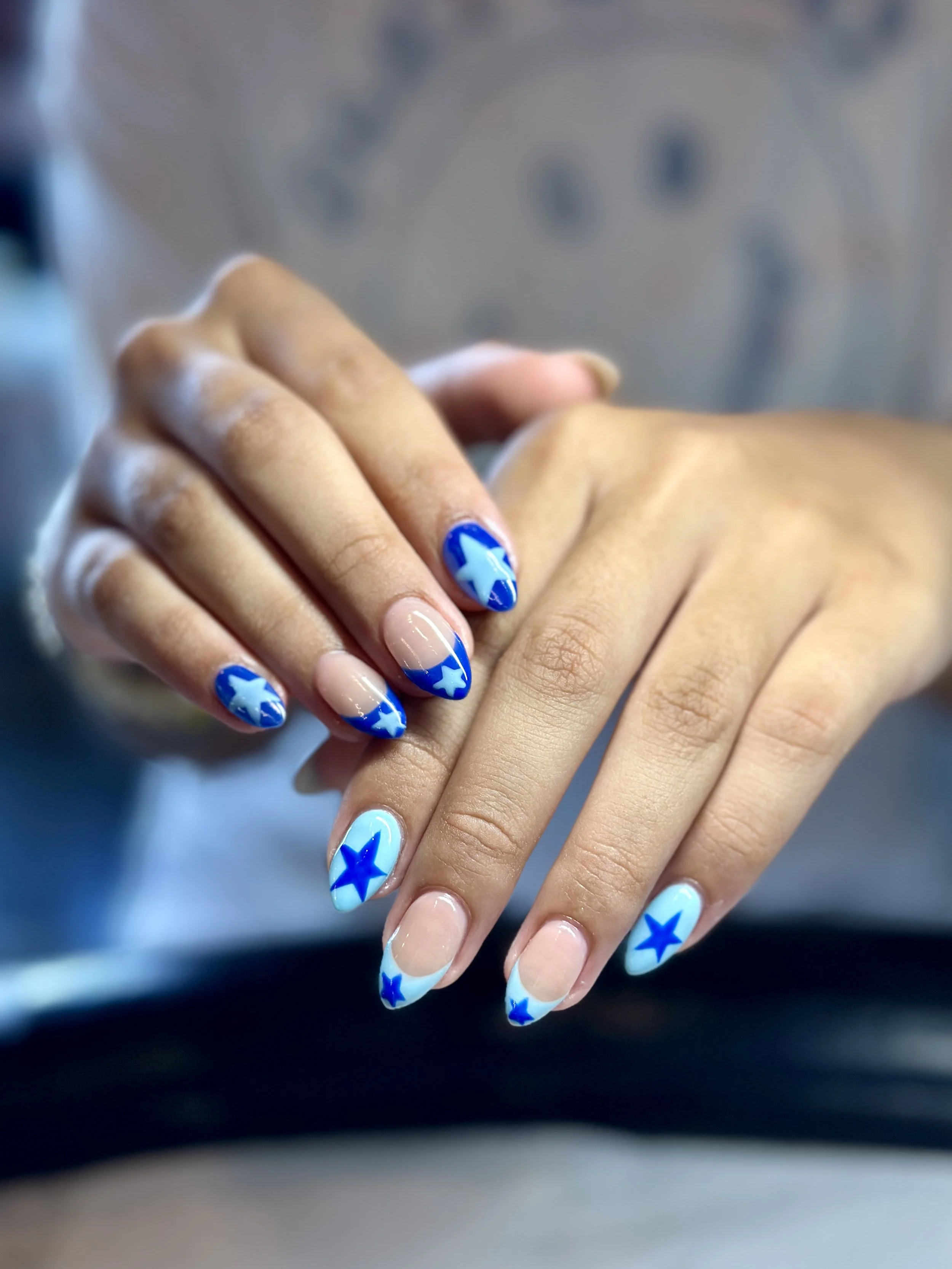 Close-up of hands with blue and white star-themed nail art, blurred background.