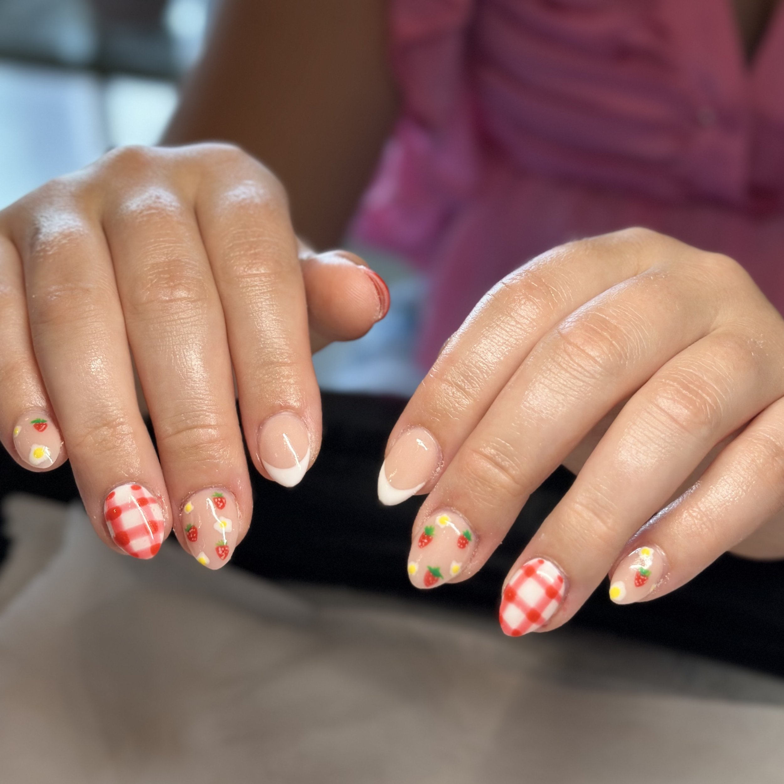 Close-up of hands with decorated nails featuring strawberries, gingham patterns, and small flowers.