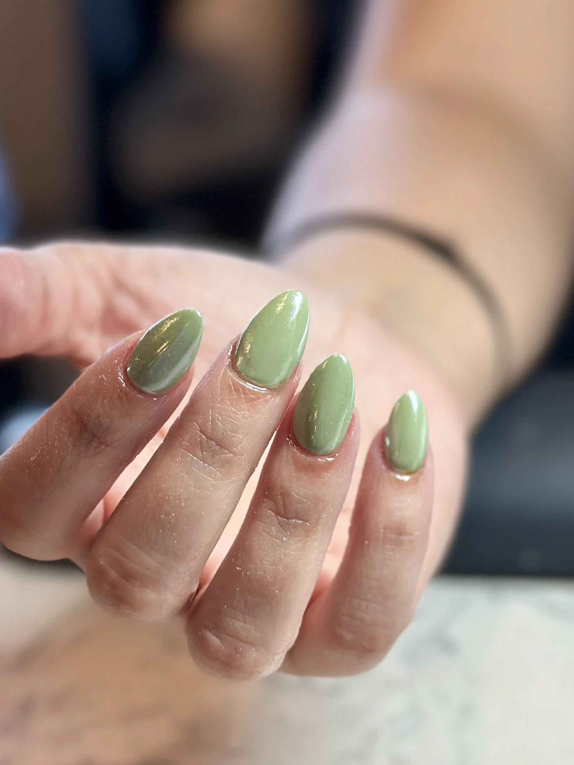Close-up of a hand with lime green manicured nails, fingers slightly curled, against a blurred background.