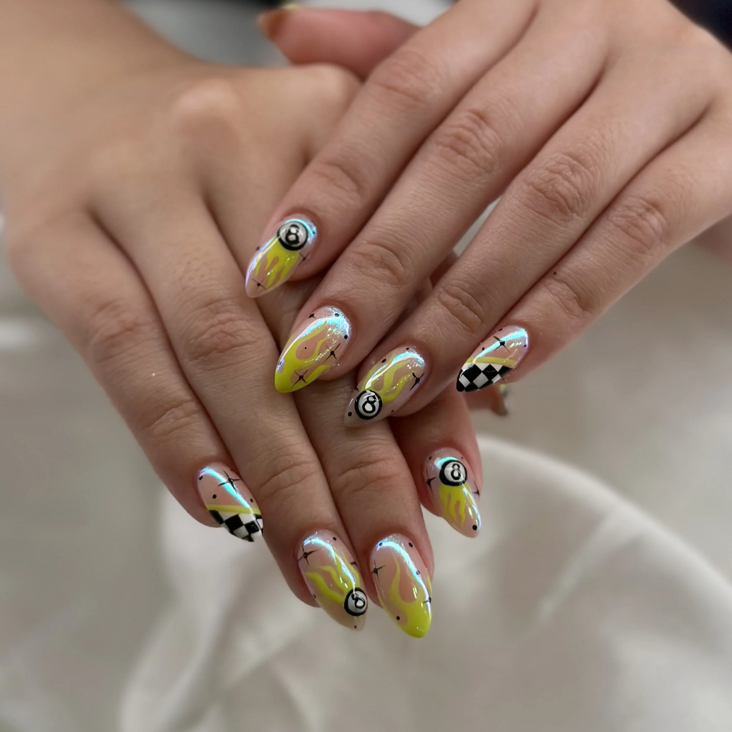 Close-up of a person's hand with colorful, decorated nails, featuring neon yellow, black and white patterns, and small decorative designs including a soccer ball and the '@' symbol.