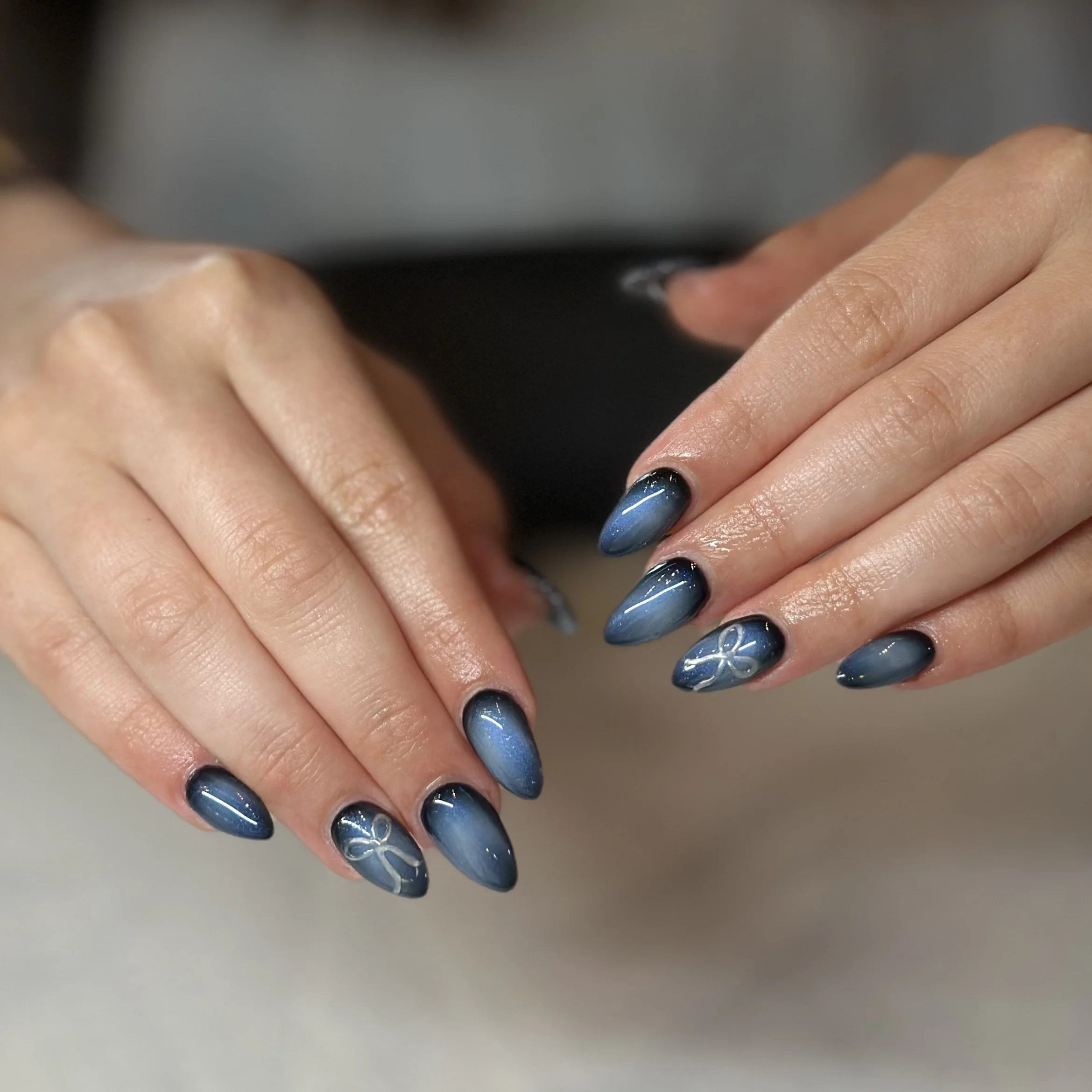 Close-up of hands with dark blue and silver manicured nails, with some nails featuring laser-style geometric designs.
