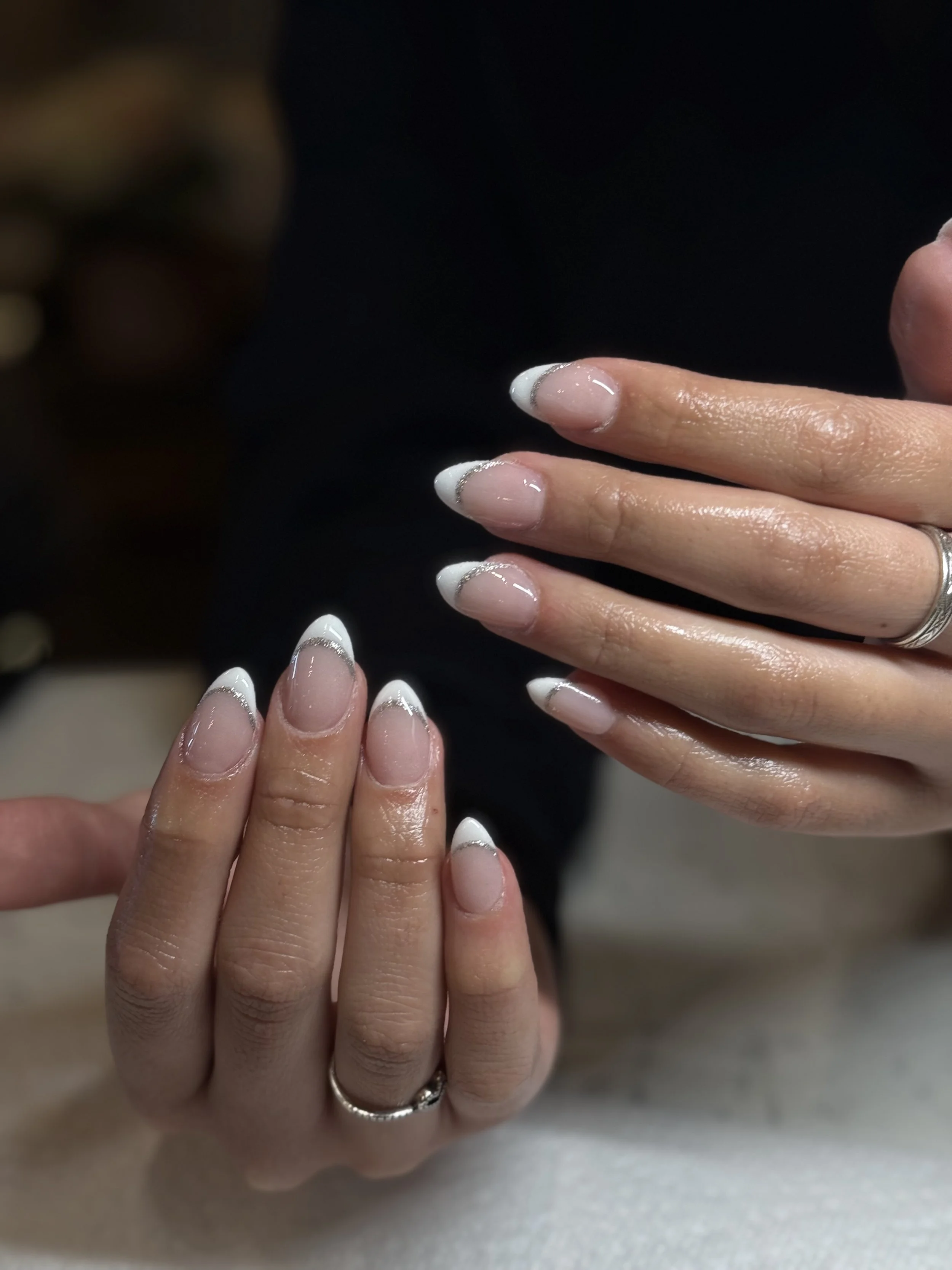 Close-up of hands with freshly manicured nails, featuring white French tips with silver accents.