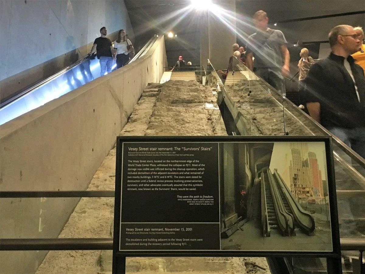 Remains of the Vesey Street stairs from the World Trade Center, displayed in a museum with an informational sign, surrounded by visitors.